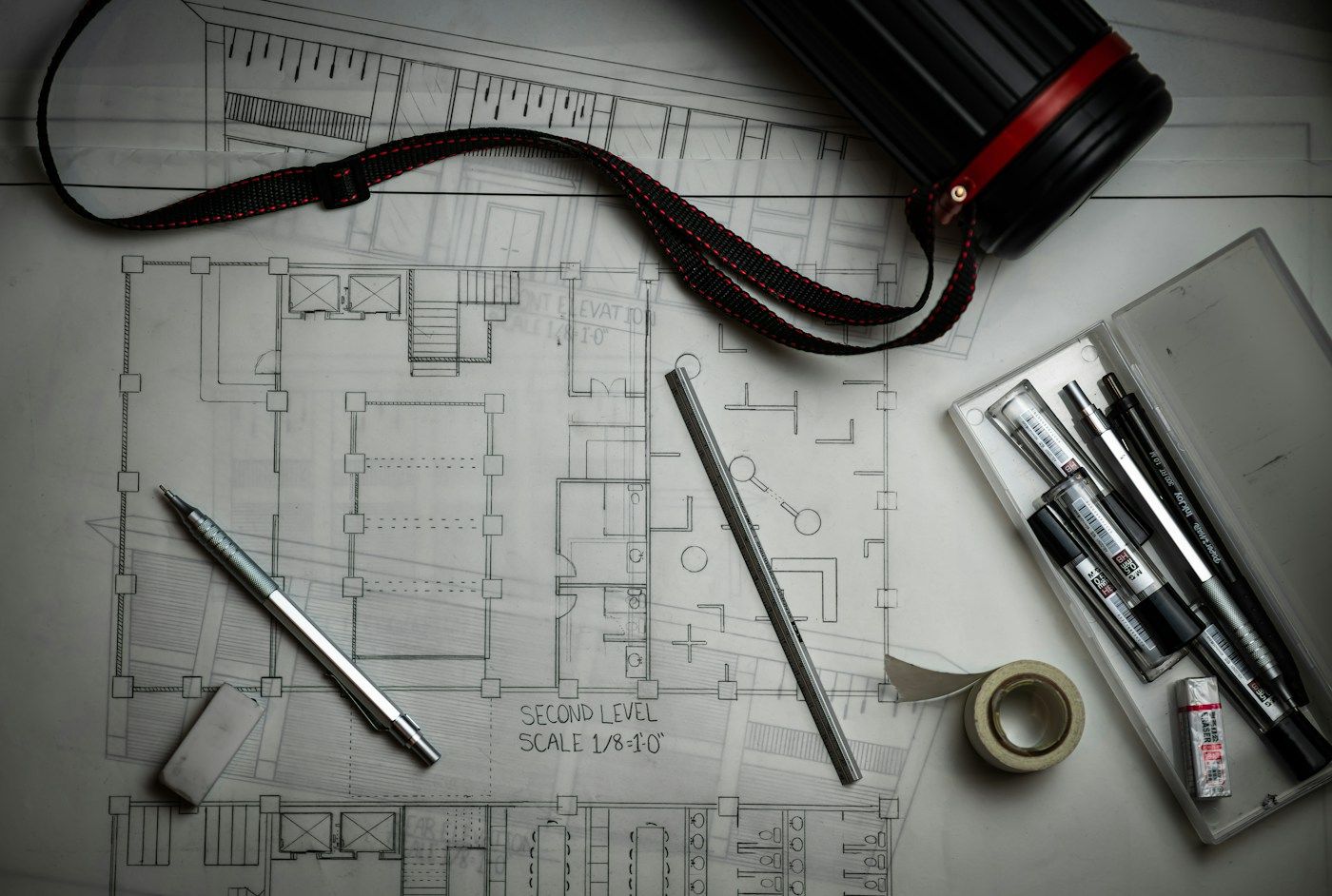 Architectural drawings on a desk with a pen, a scale rule and drafting tools